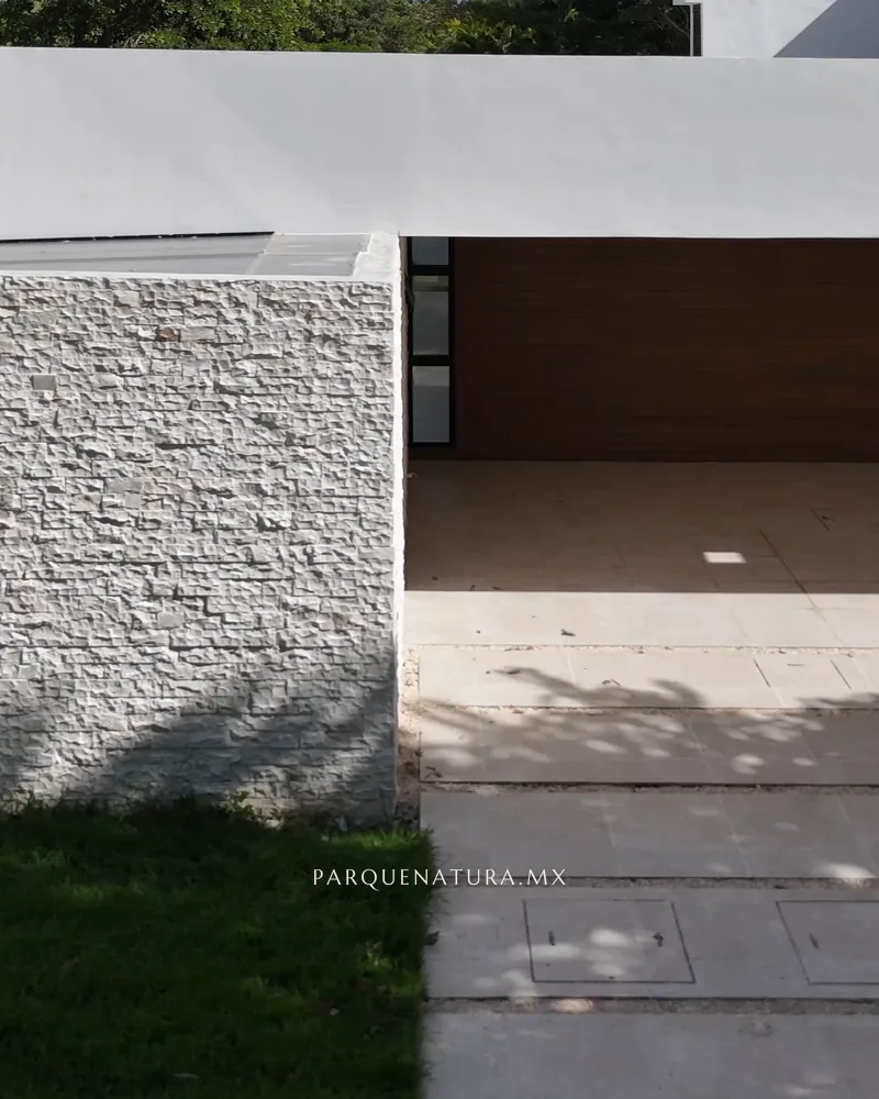 Fachada de la Casa 208 con muro de piedra y cochera techada