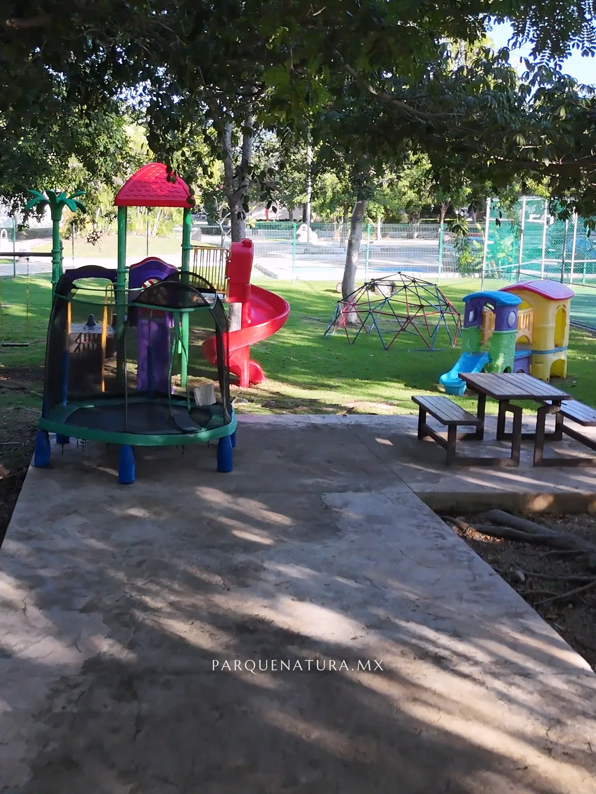 Juegos infantiles entre árboles grandes, junto a un andador
