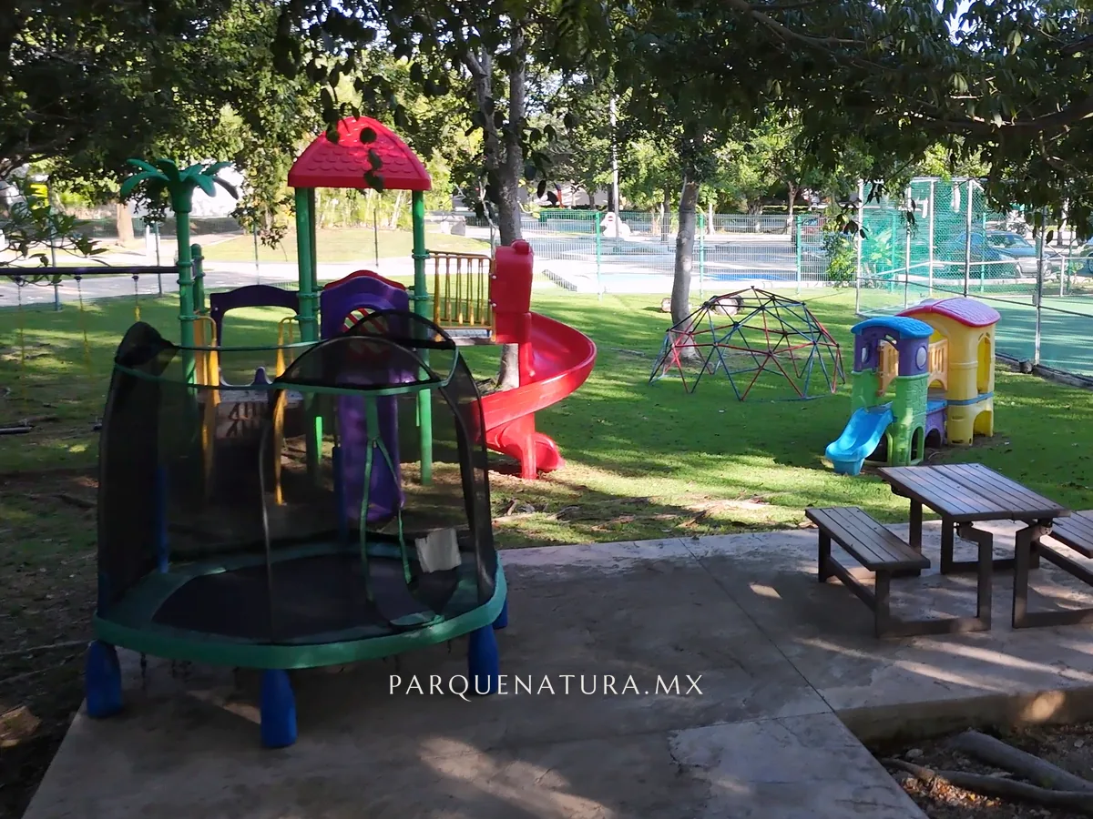 Juegos infantiles entre árboles grandes, junto a un andador